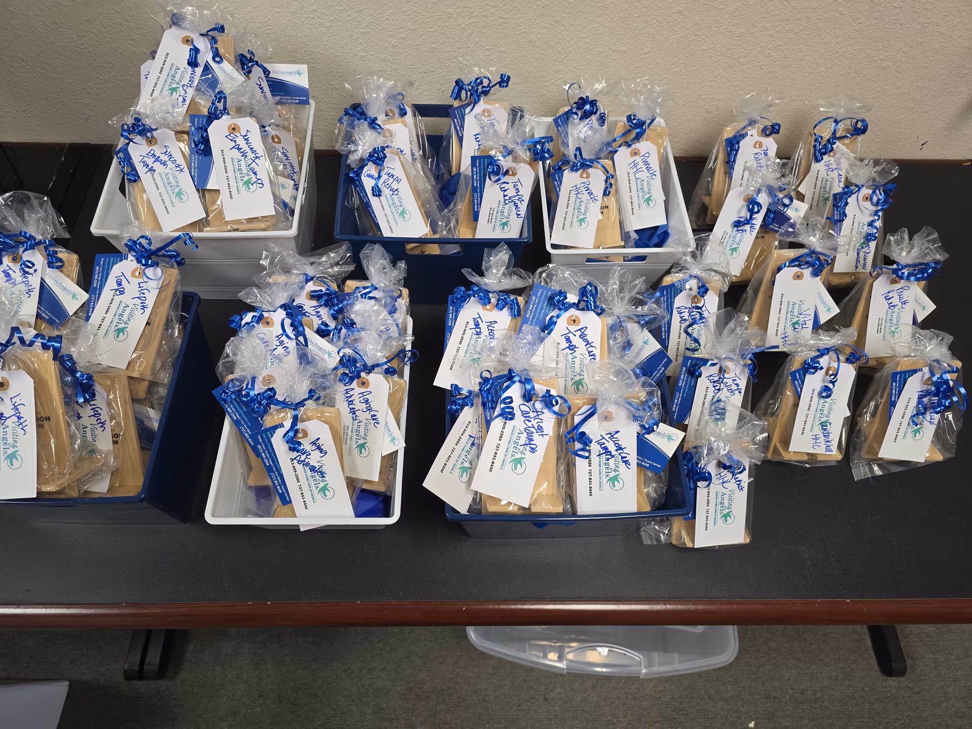 Gift bags with tags and blue ribbons arranged in blue and white bins on a table