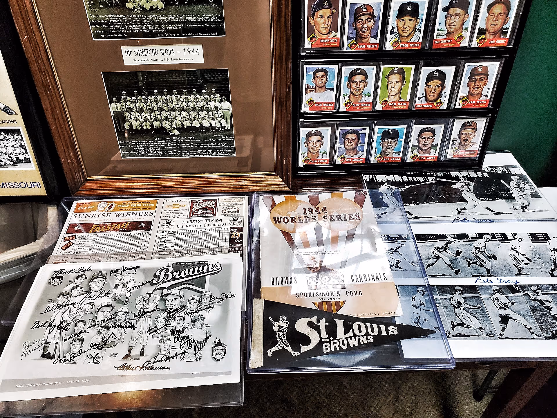 A display of vintage baseball memorabilia related to the 1944 World Series featuring the St. Louis Browns and St. Louis Cardinals. The display includes framed team photos, baseball cards, a pennant, a program, and black-and-white action photos from the games.