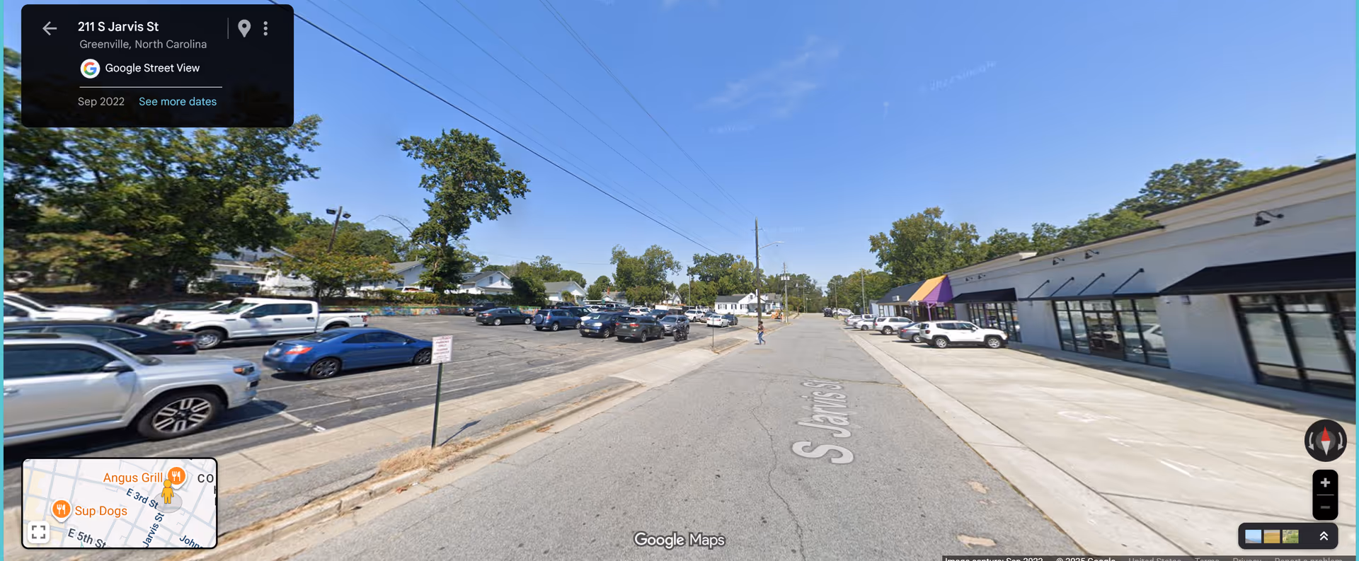 Wide street view of a strip mall with parked cars and storefronts.