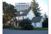 Front exterior of a white facility building with trees and a taller structure in background.