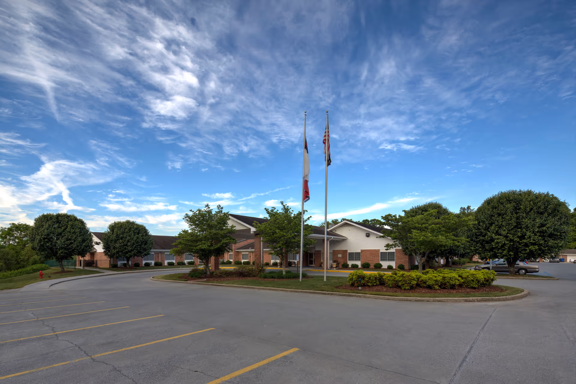 Front exterior of Lakebridge - A Waters Community with flagpoles, landscaping, and parking.