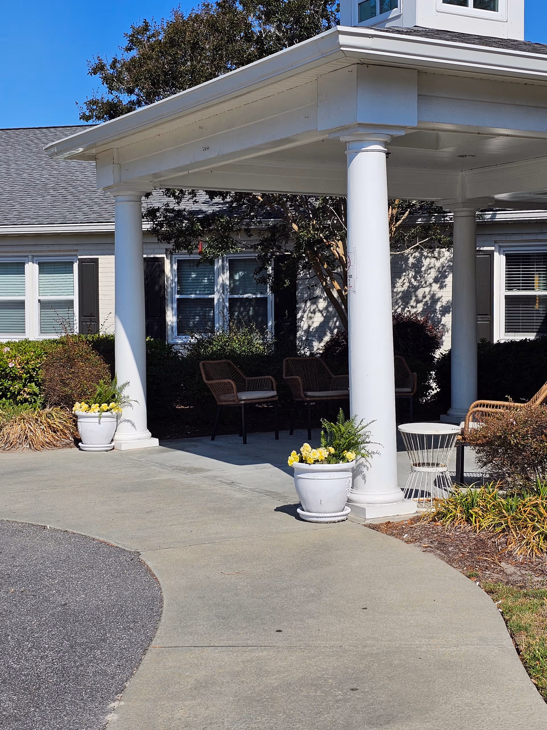 Myrtle Beach Manor entrance with white columns, seating, and potted flowers outdoors.