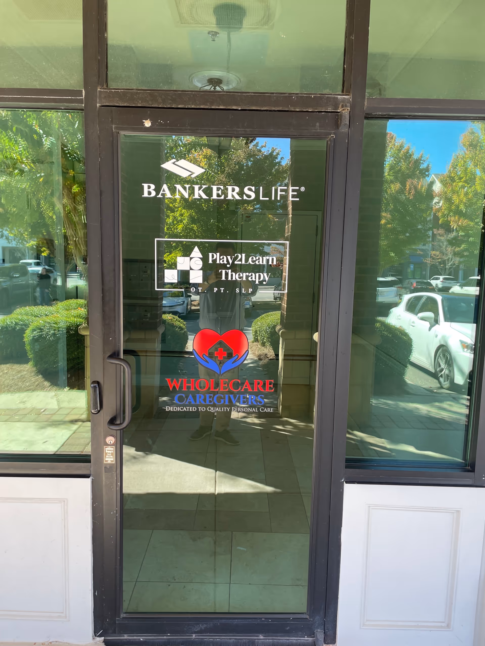 Glass entrance door displaying logos for Bankers Life, Play2Learn Therapy, and Wholecare Caregivers.