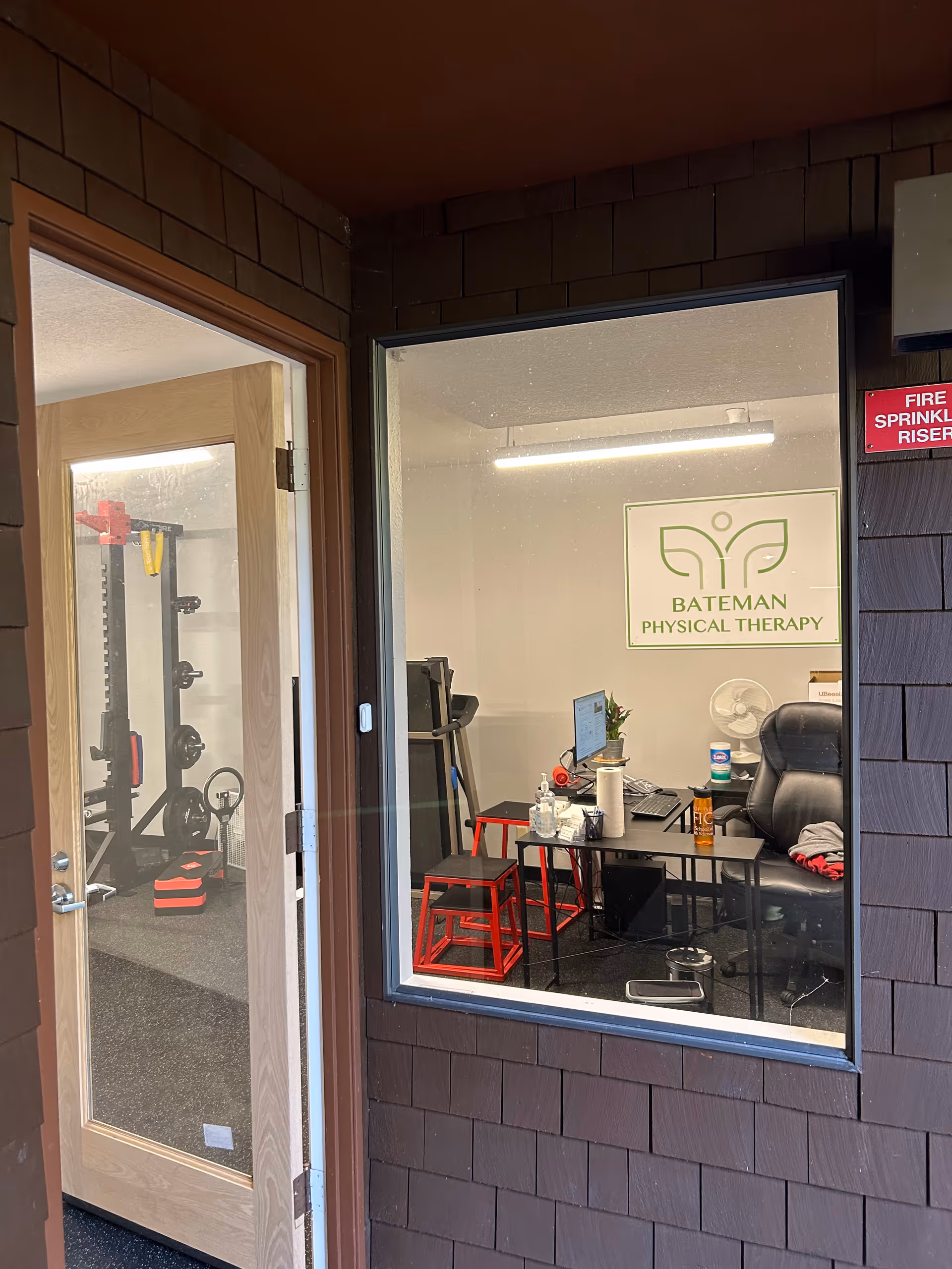 Inside Bateman Physical Therapy, an office desk with computer overlooks a small gym area.