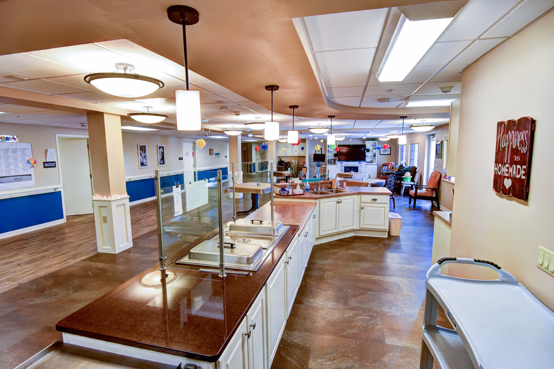 Open serving kitchen and communal dining area with a long service counter, pendant lights, and seating with a television.
