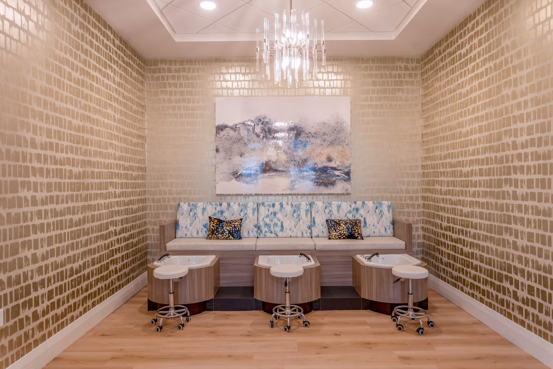 Interior pedicure station with sinks, stools, and a cushioned bench along patterned walls.