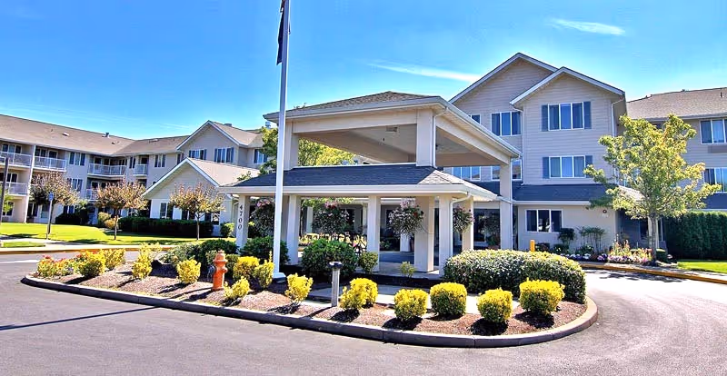 Exterior view of a senior living facility with a covered entrance and landscaped drive.