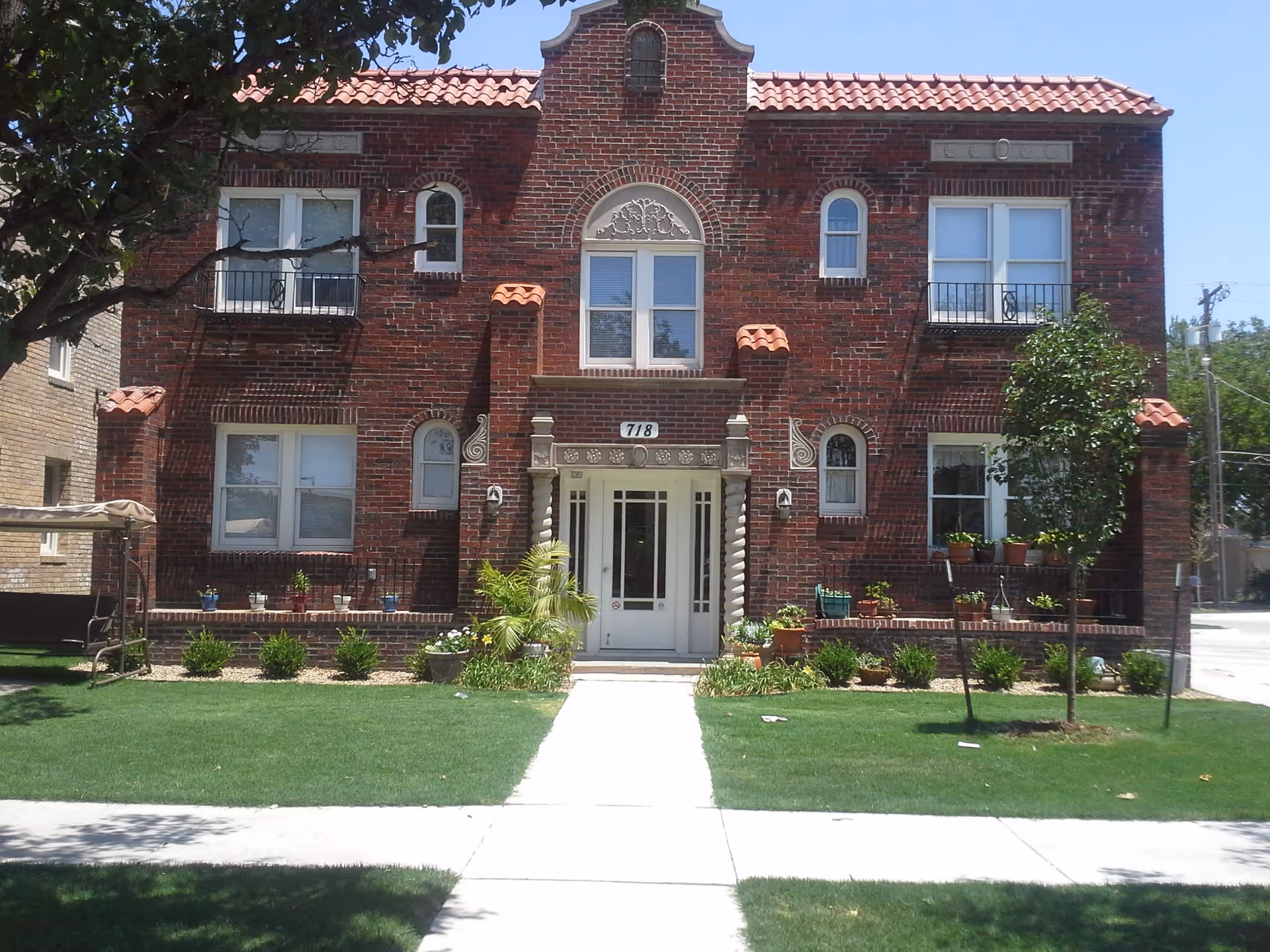 Brick two-story apartment building with a central entrance labeled 718 and a landscaped front lawn.