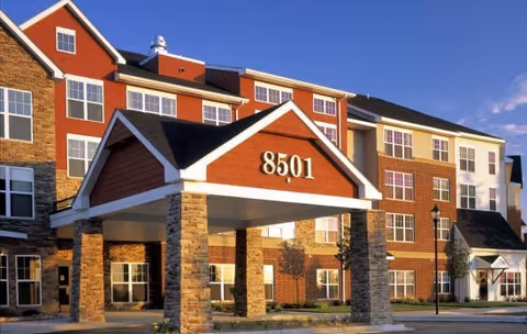 Red-brick senior living campus building with a covered entrance and address 8501