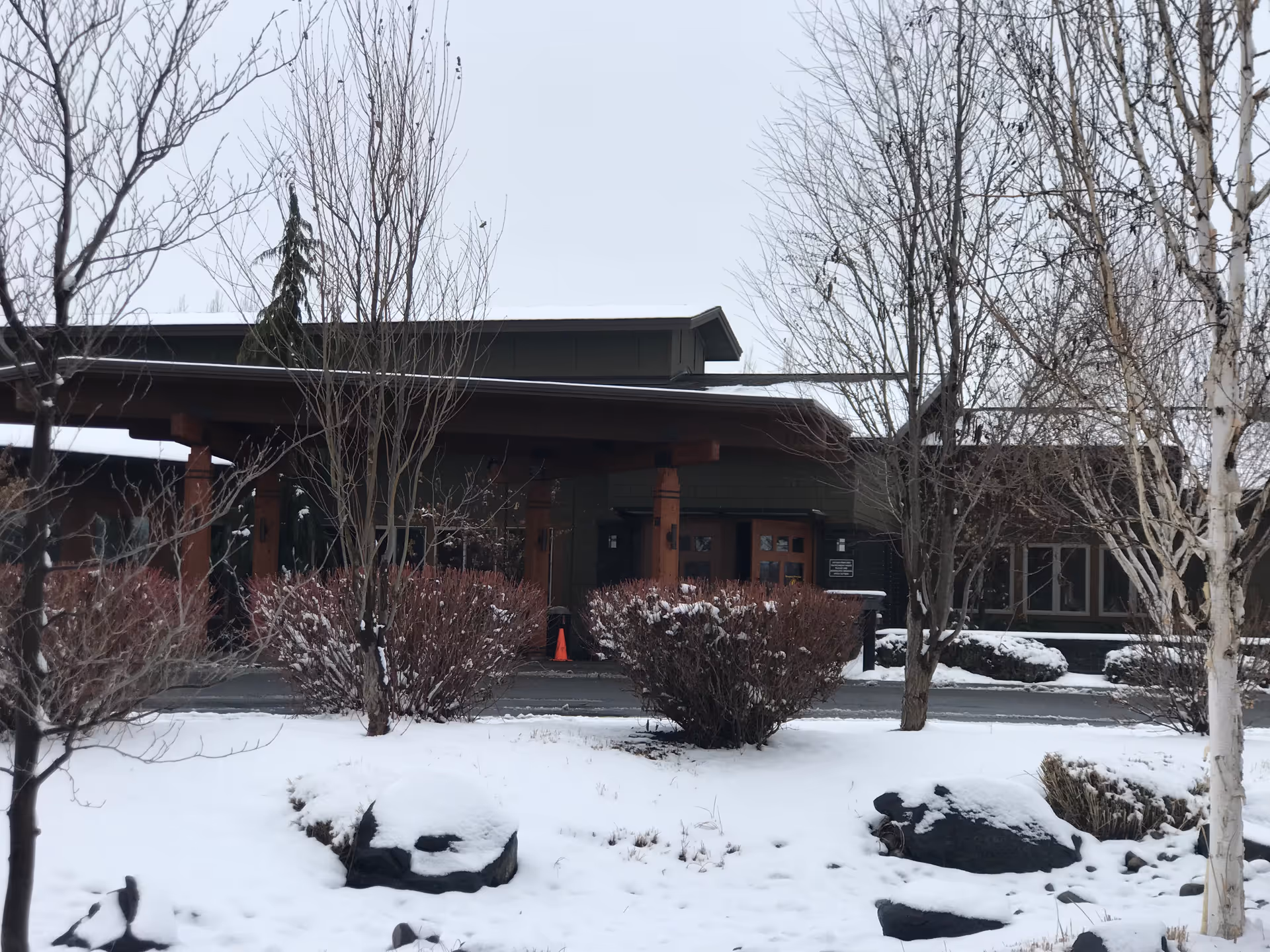 Snow covered building front with bare trees and a central entrance.