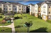Sunlit senior living facility with beige exterior, green courtyard, gazebo, and benches.