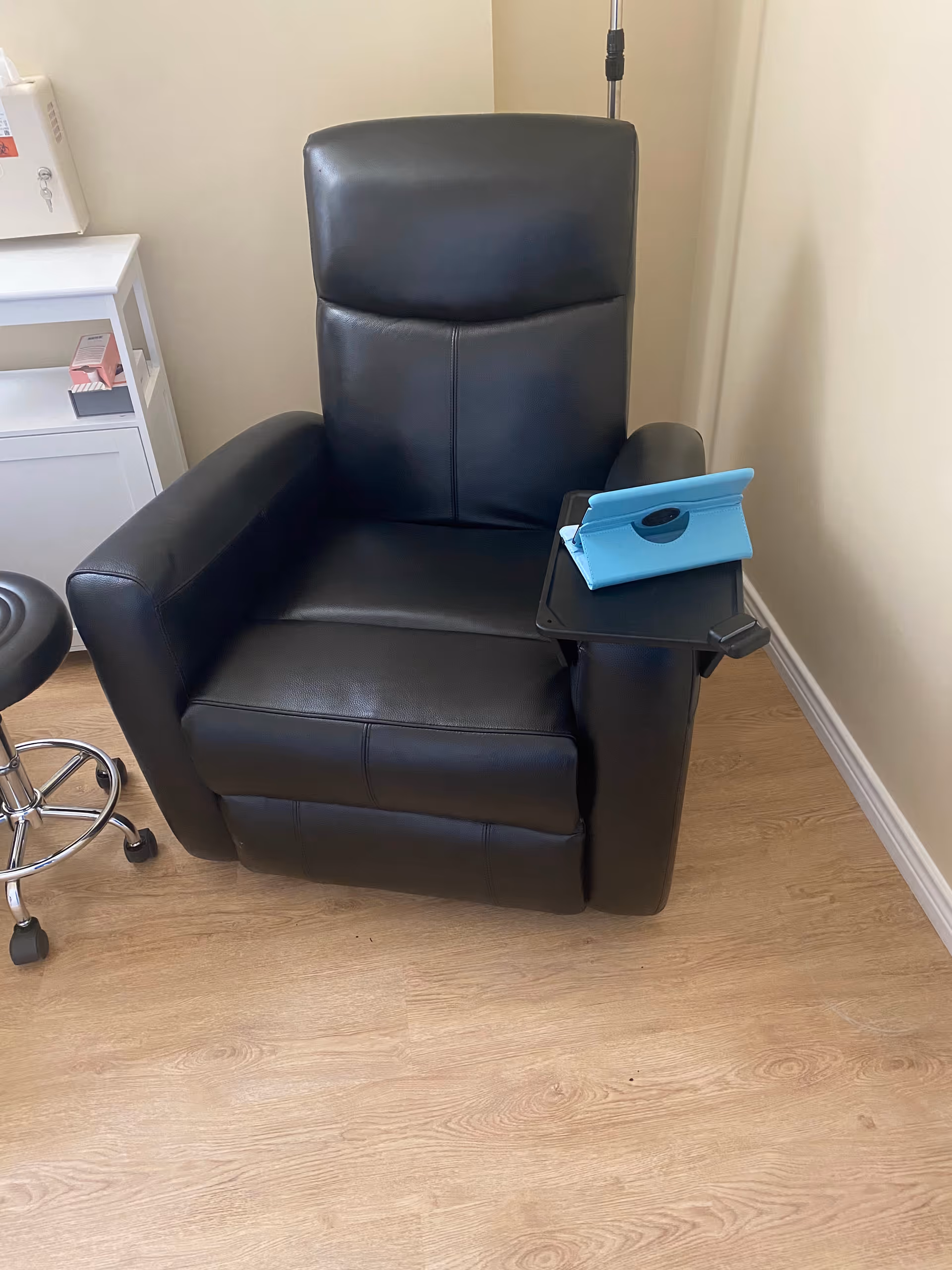 Black leather recliner with a small side tray in an infusion room.