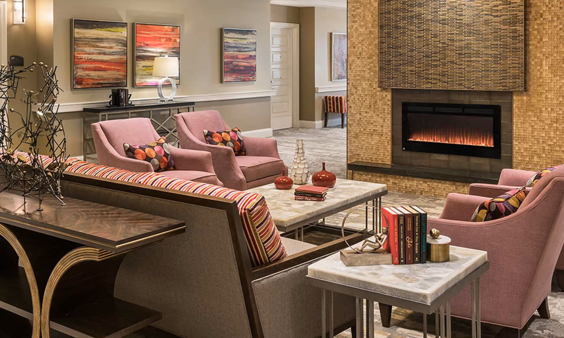 Luxurious lounge area with pink seating, marble coffee tables, abstract art, and a fireplace.