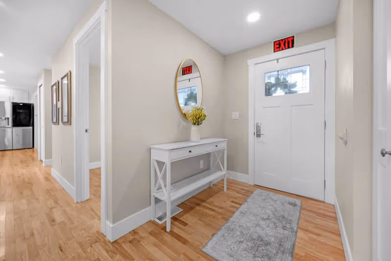 Bright hallway with a console table, mirror, vase, and an exit door.
