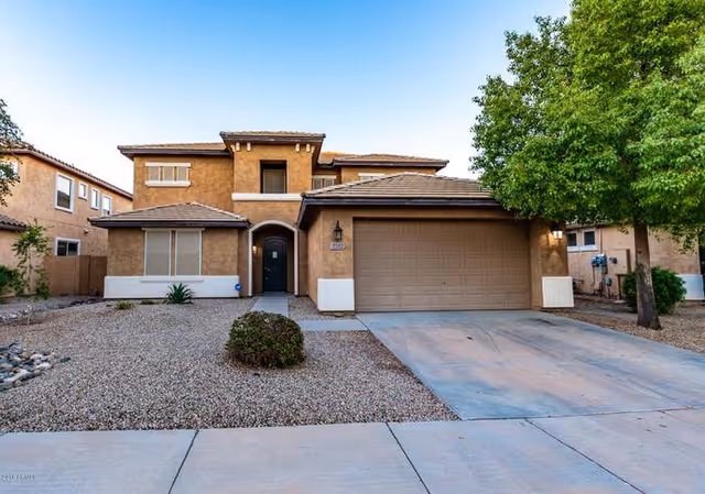 Front view of a two-story stucco house with a two-car garage and desert landscaping.