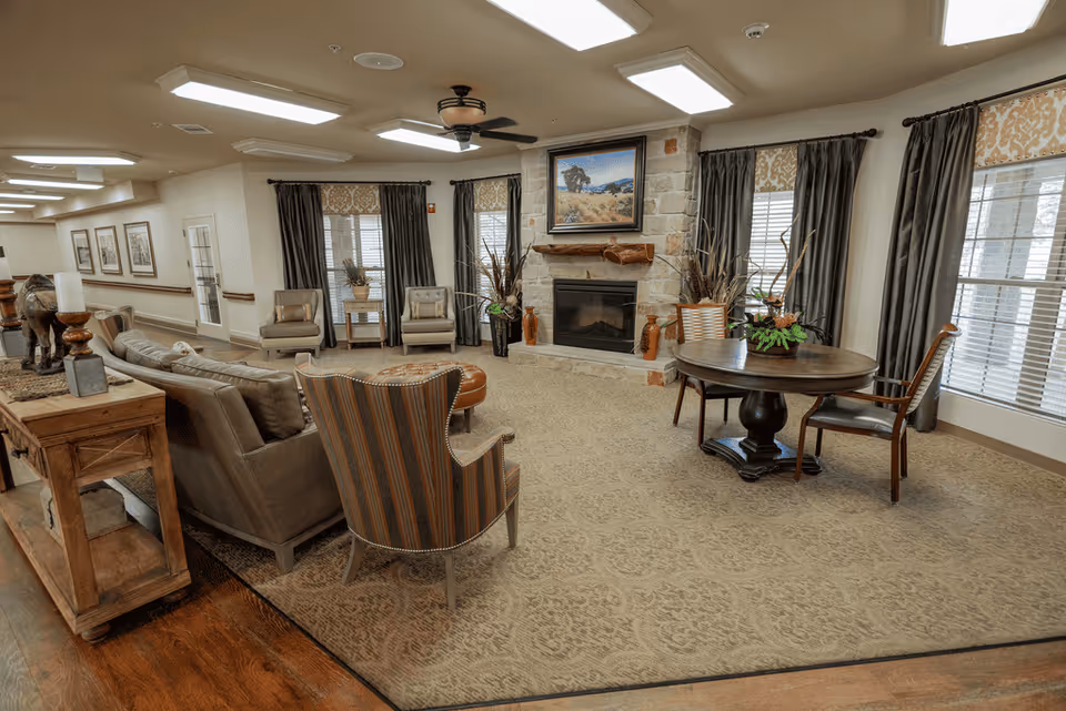 Spacious senior living lounge with sofas, chairs, a fireplace, and a round table.
