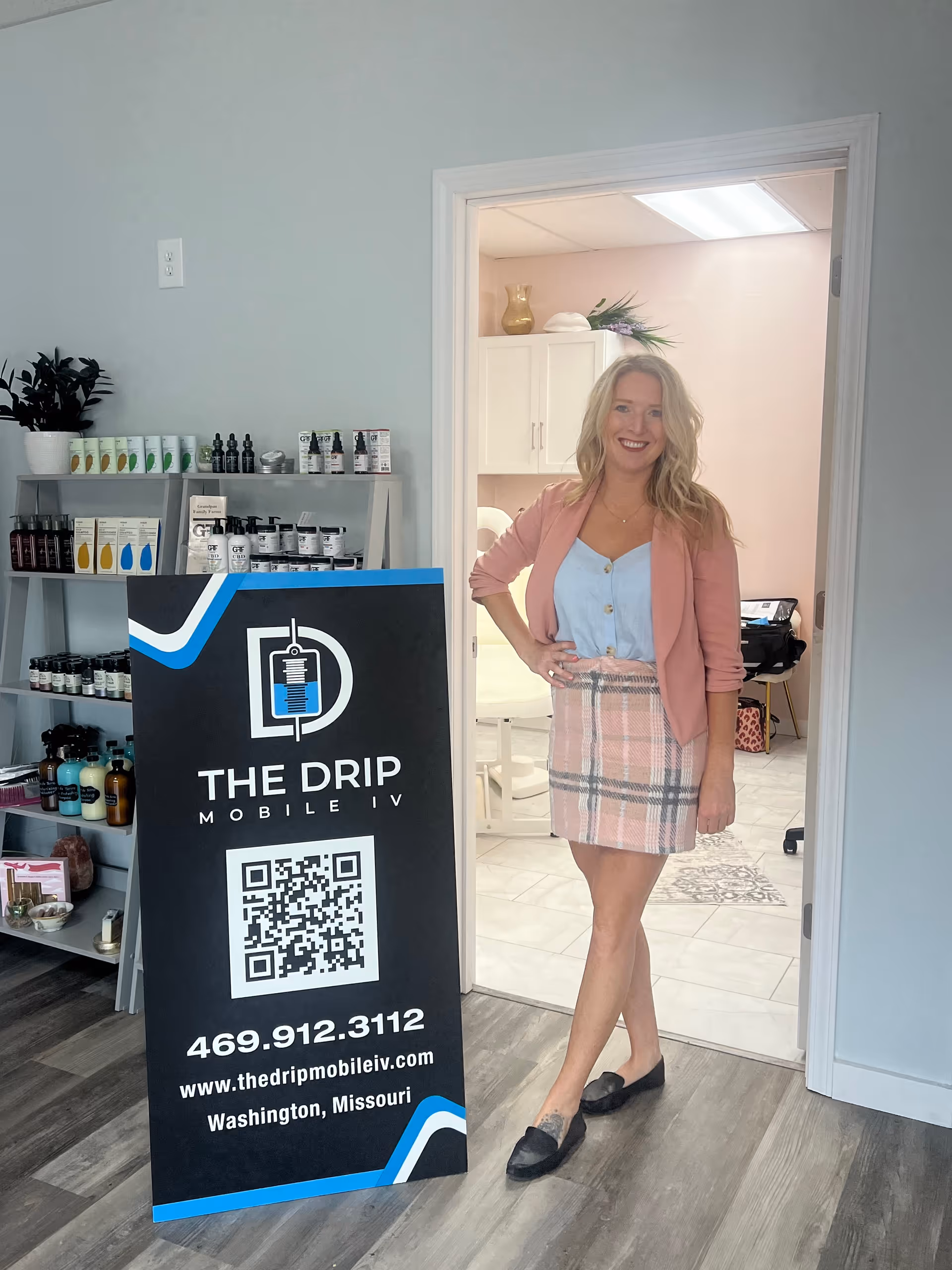 Smiling woman stands by a doorway beside The Drip Mobile IV sign.