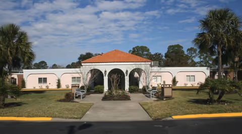 Exterior view of Senior Care Center - Brunswick with arches, lawn, and palm trees.
