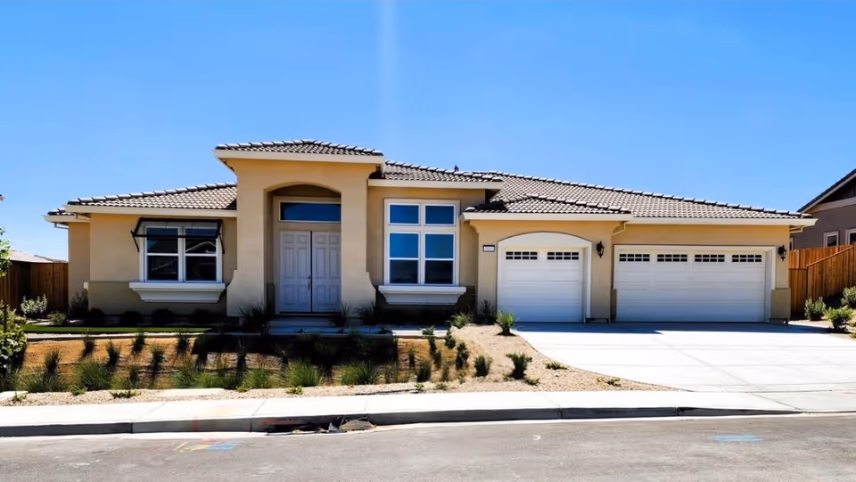 Beige, single-story building with a three-car garage and desert landscaping.