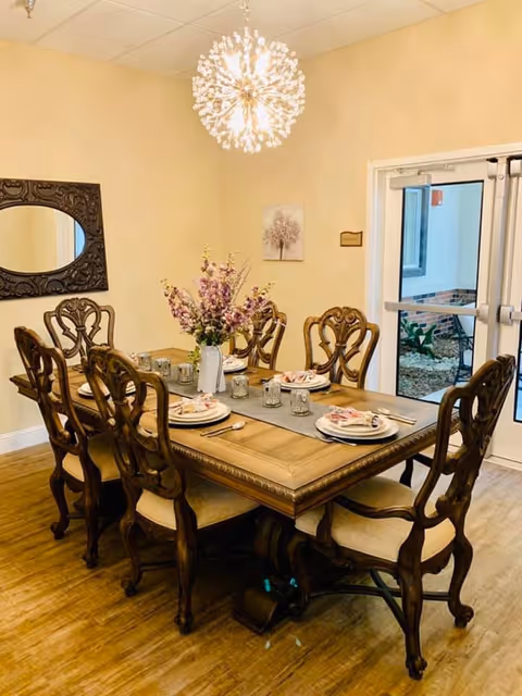 Elegant dining room with a wooden table set for six, floral centerpiece, ornate chairs, and a chandelier near double doors.