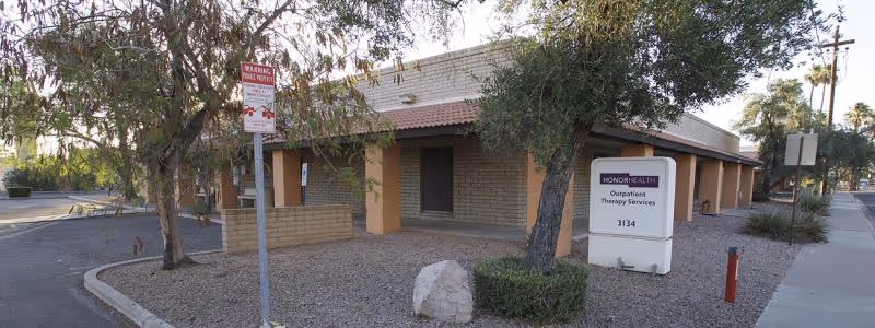 Exterior view of a single-story building with a sign, trees, and gravel landscaping.