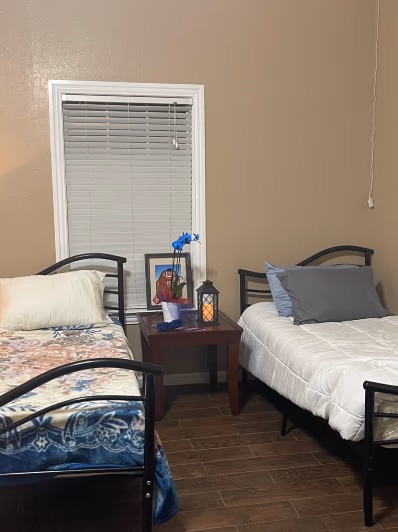Two twin beds with a nightstand between them in a beige-walled bedroom.