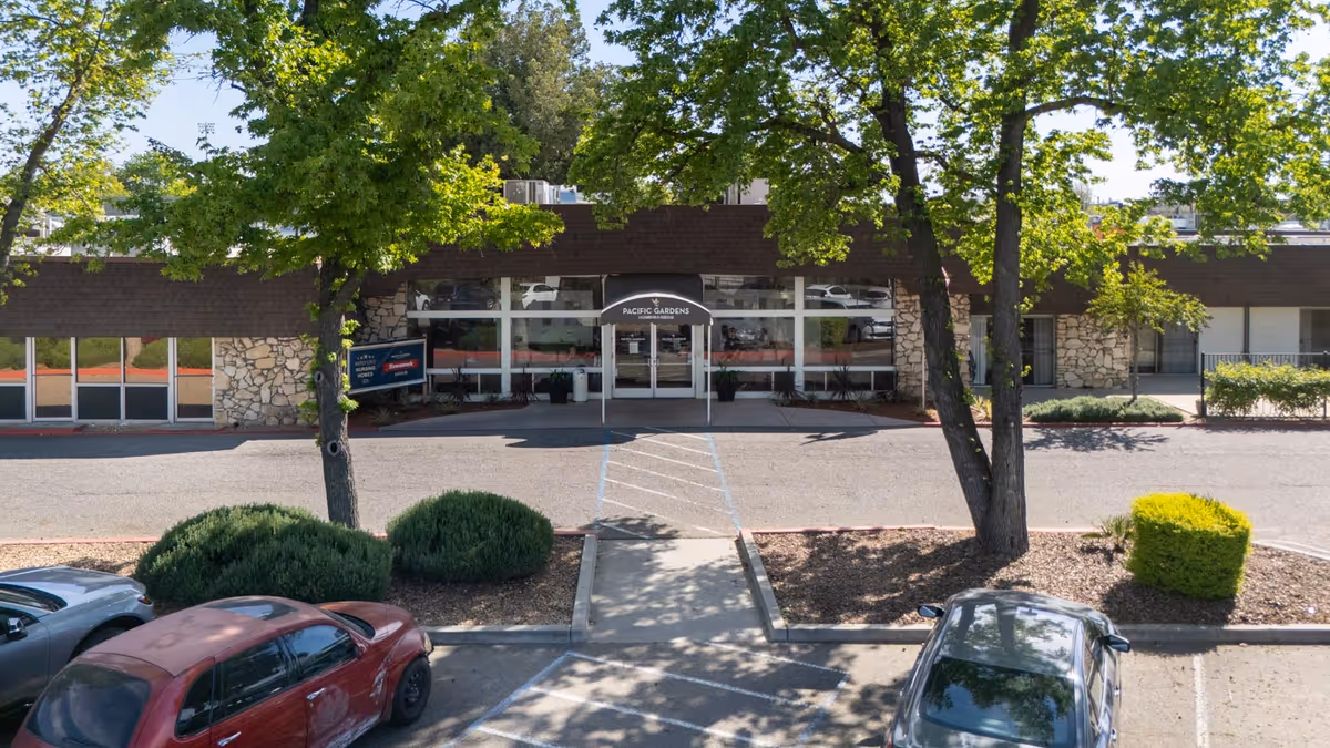 Exterior view of the Pacific Gardens Nursing and Rehabilitation Center entrance, with trees and parked cars.