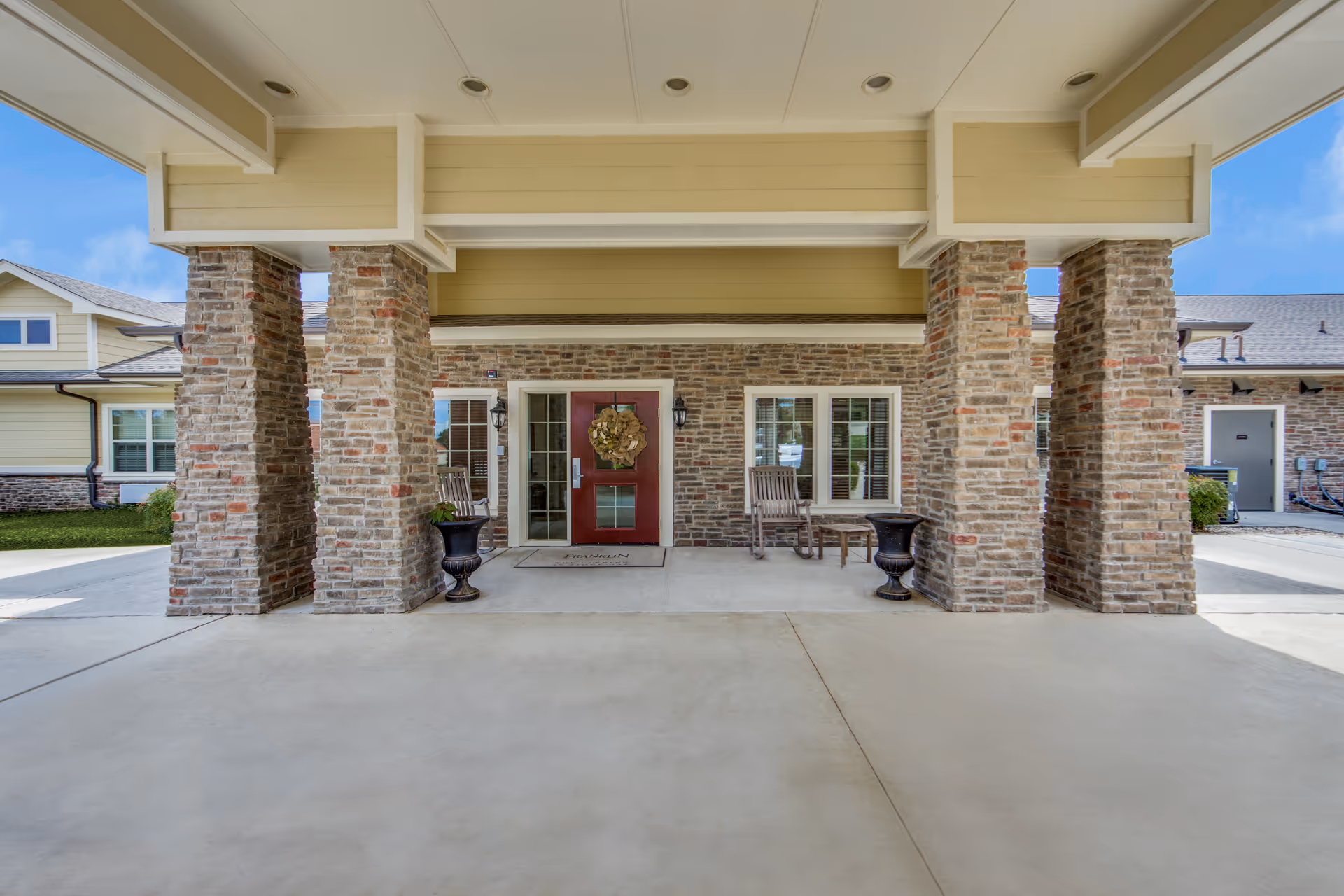 Exterior entrance with stone pillars and seating at The Landing at Stone Oak Memory Care.