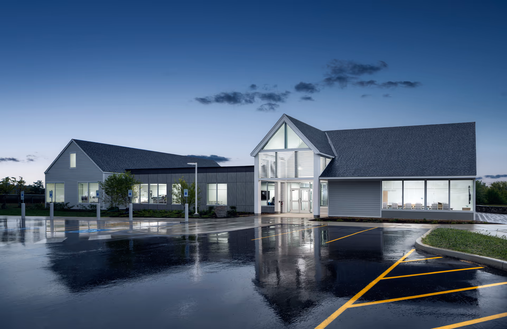 Exterior view of a modern hospice facility with glass entrance and wet parking lot.