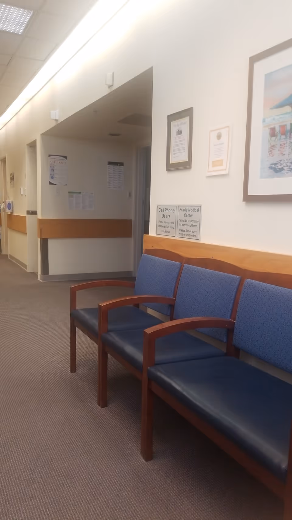 Indoor hallway with blue upholstered chairs along the wall and framed notices.