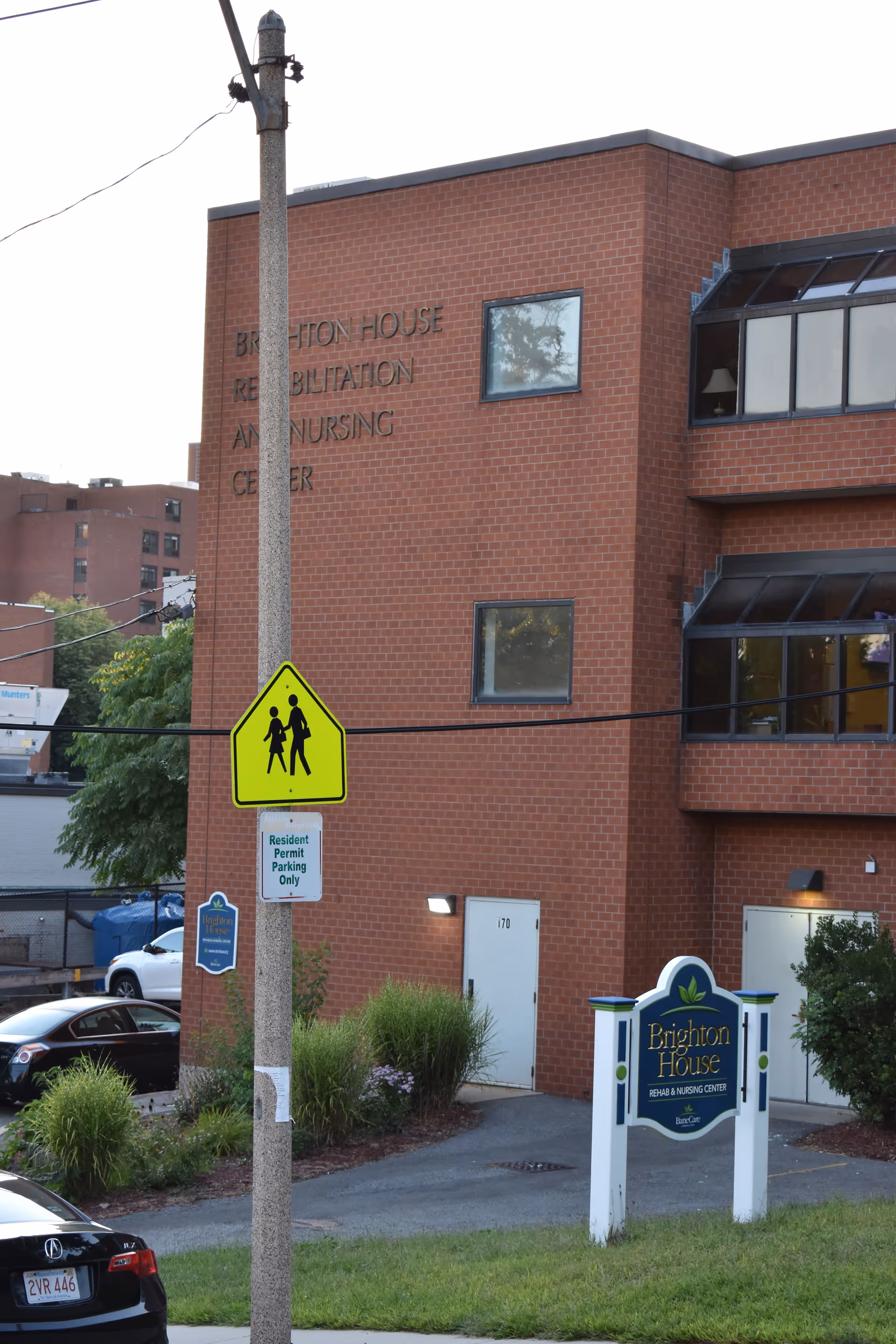 Brick Brighton House Rehabilitation and Nursing Center building with signage and a pedestrian crossing sign.