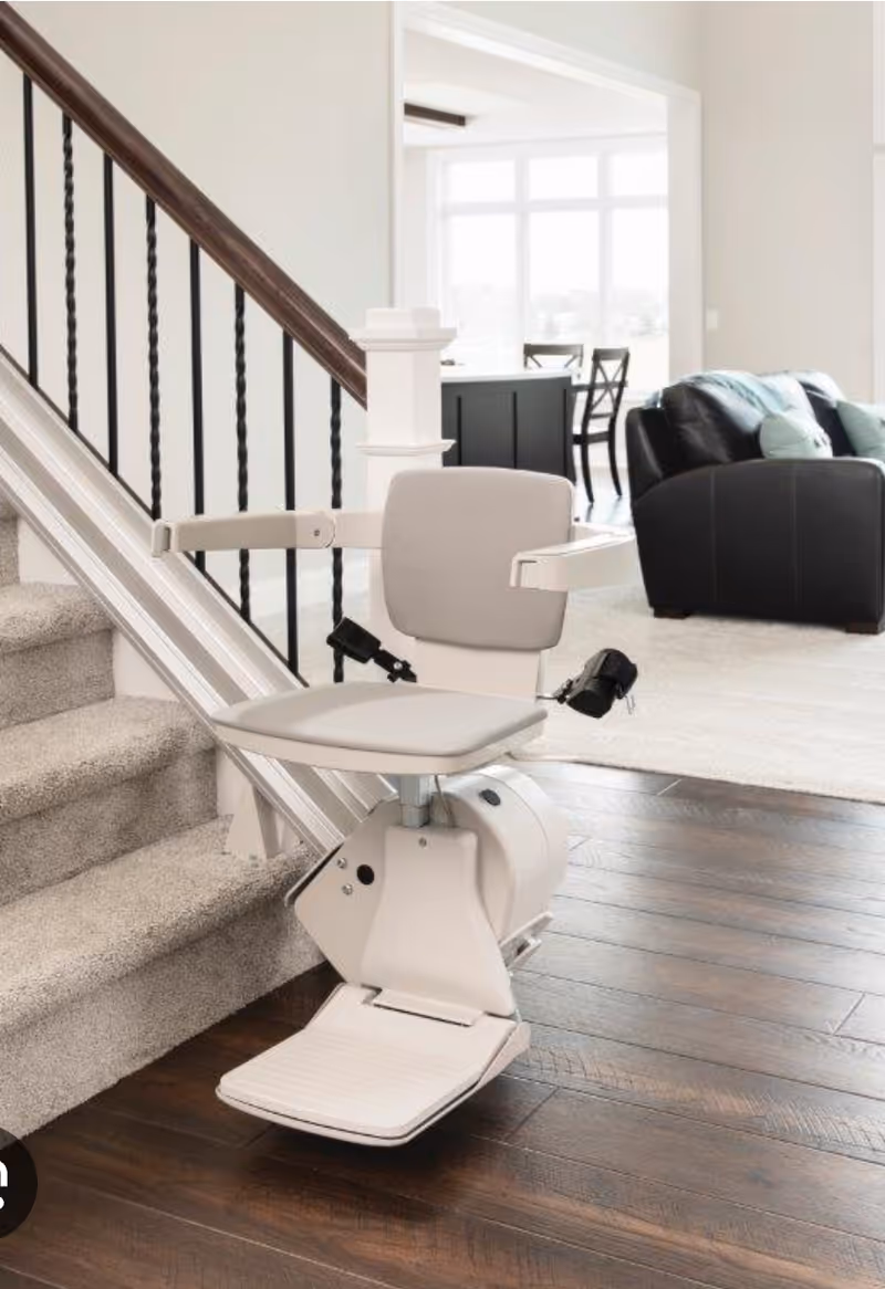 White stair lift installed beside a staircase in a bright, open living area.