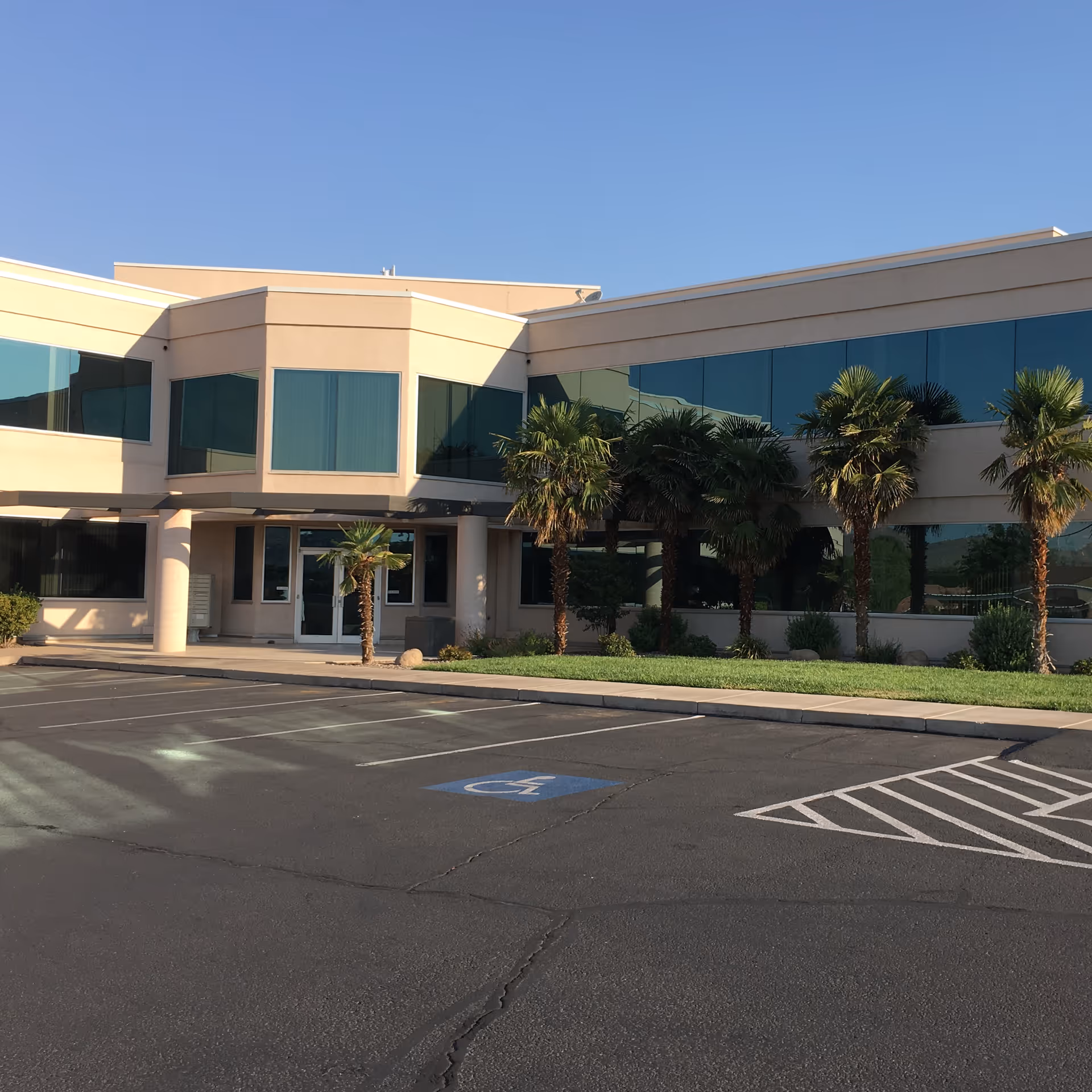 Exterior view of a modern medical building with glass windows, palm trees, and parking.