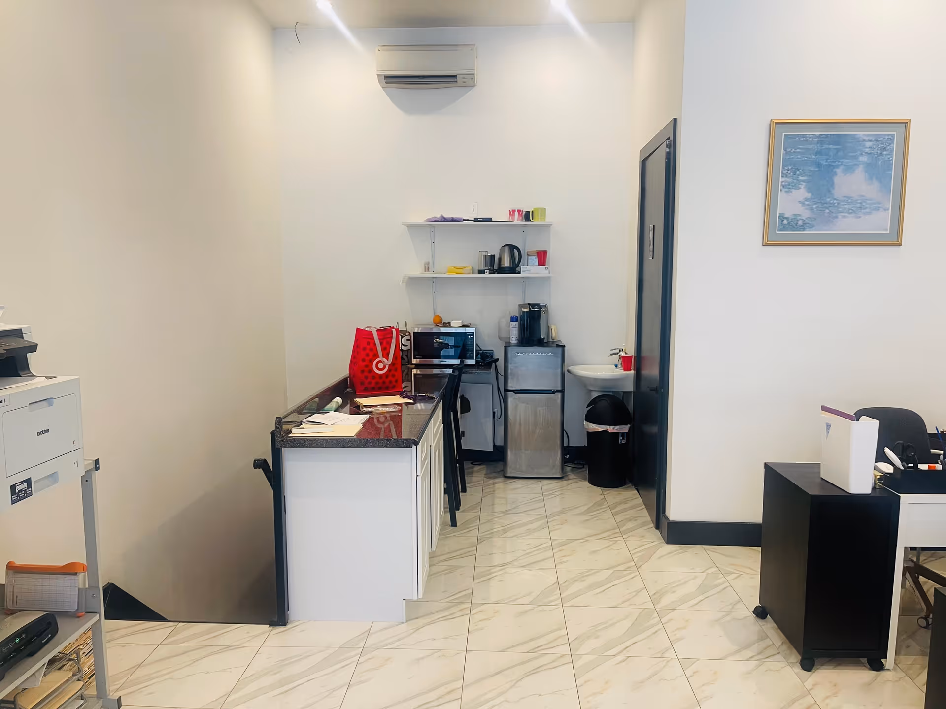 Small staff kitchenette with coffee setup, shelves, a printer desk, and a chair.