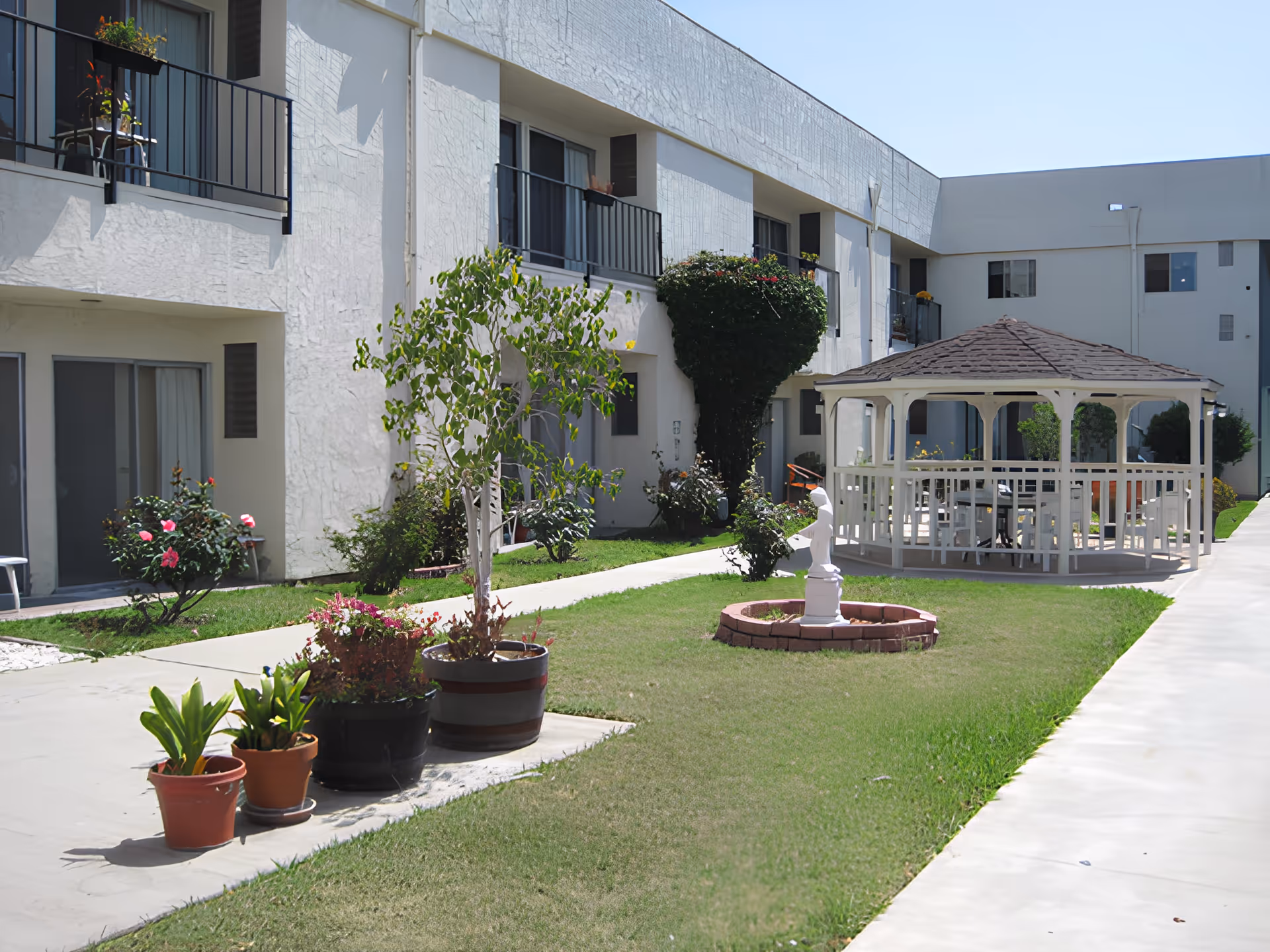 Courtyard of a white two-story retirement building featuring potted plants, a gazebo, and a small statue fountain.