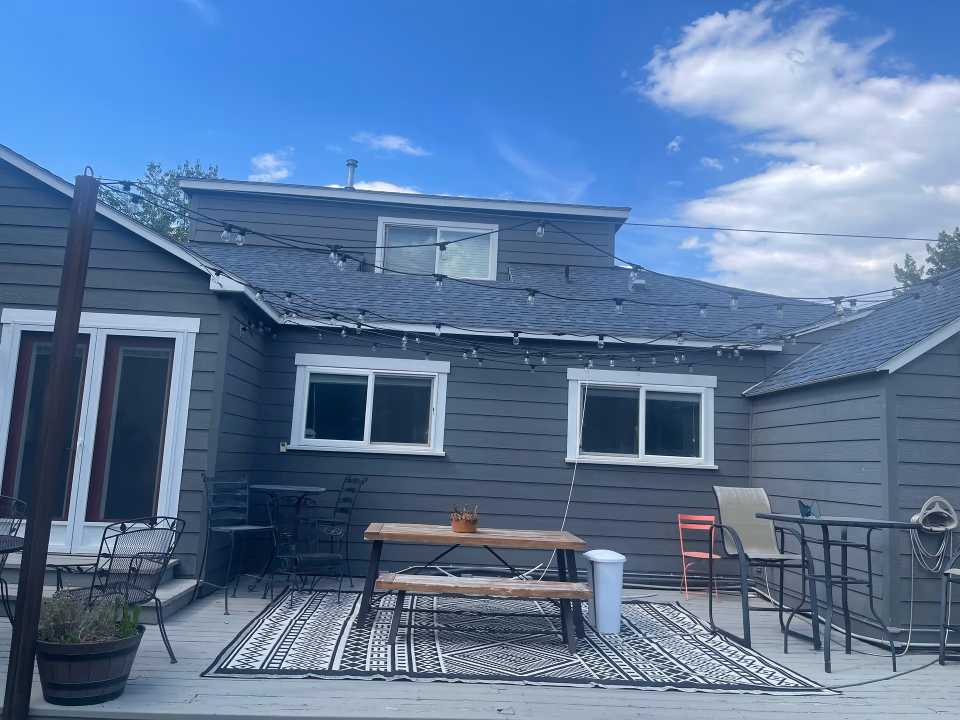 Gray exterior of a senior living facility with string-lights, a wooden deck, and outdoor furniture.
