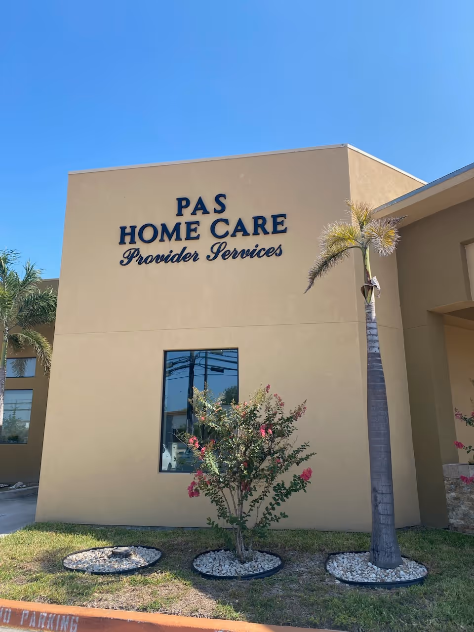 Front view of a beige Pas Home Care building with a palm tree and sign.