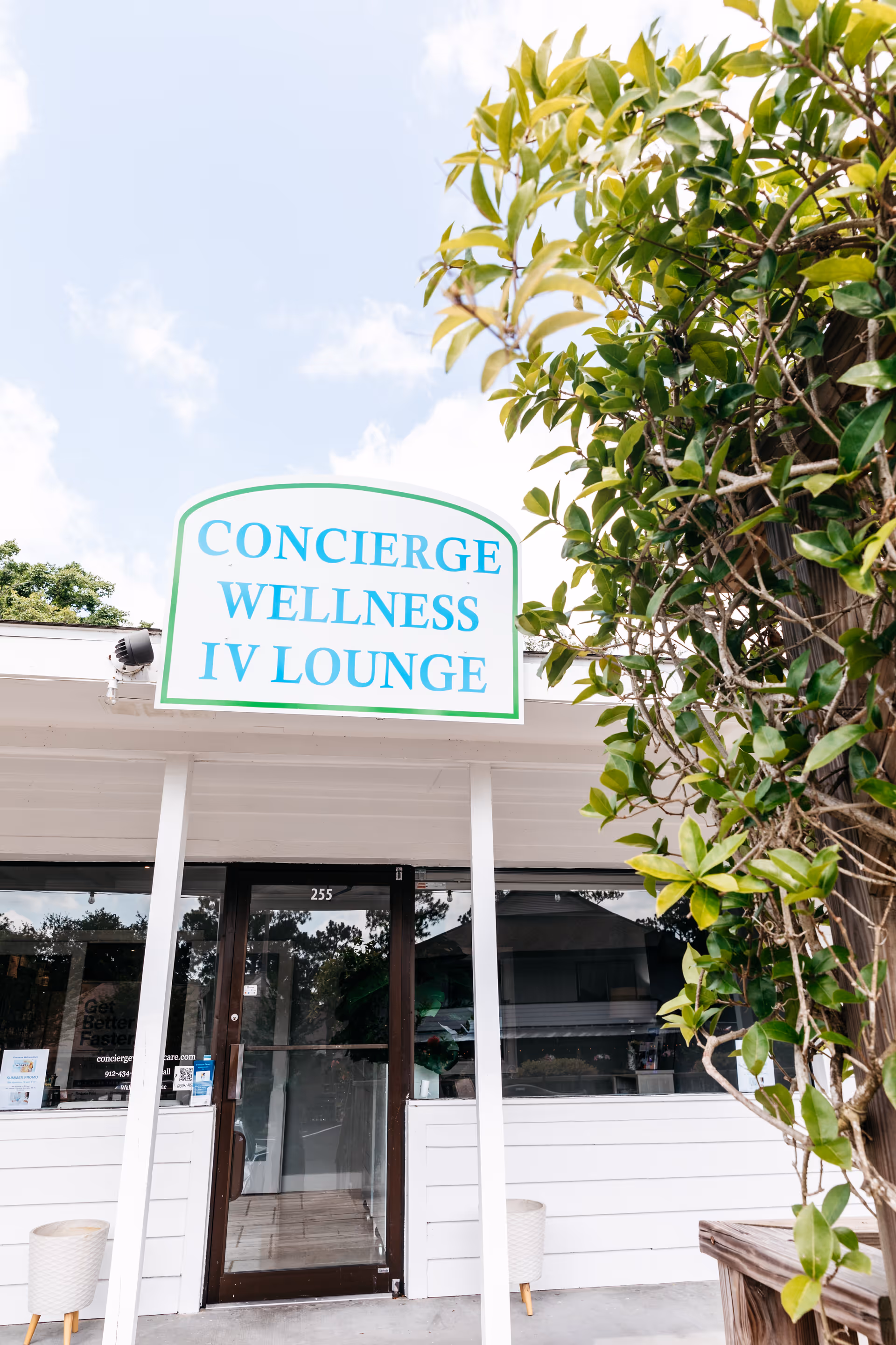 Front entrance of Concierge Wellness IV Lounge with glass doors and greenery.