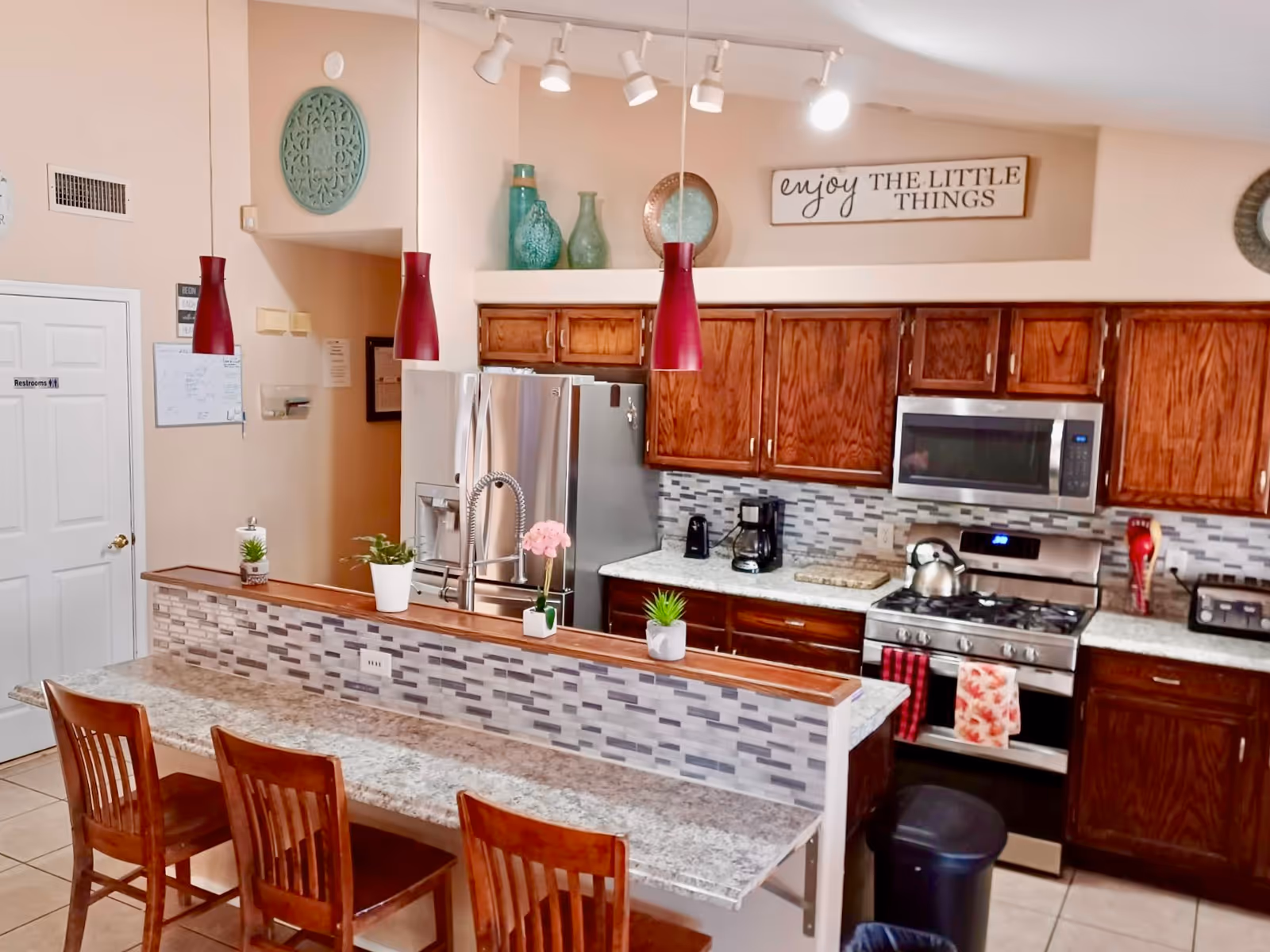 Open kitchen with island, bar seating, stainless appliances, and decorative accents in a care home.