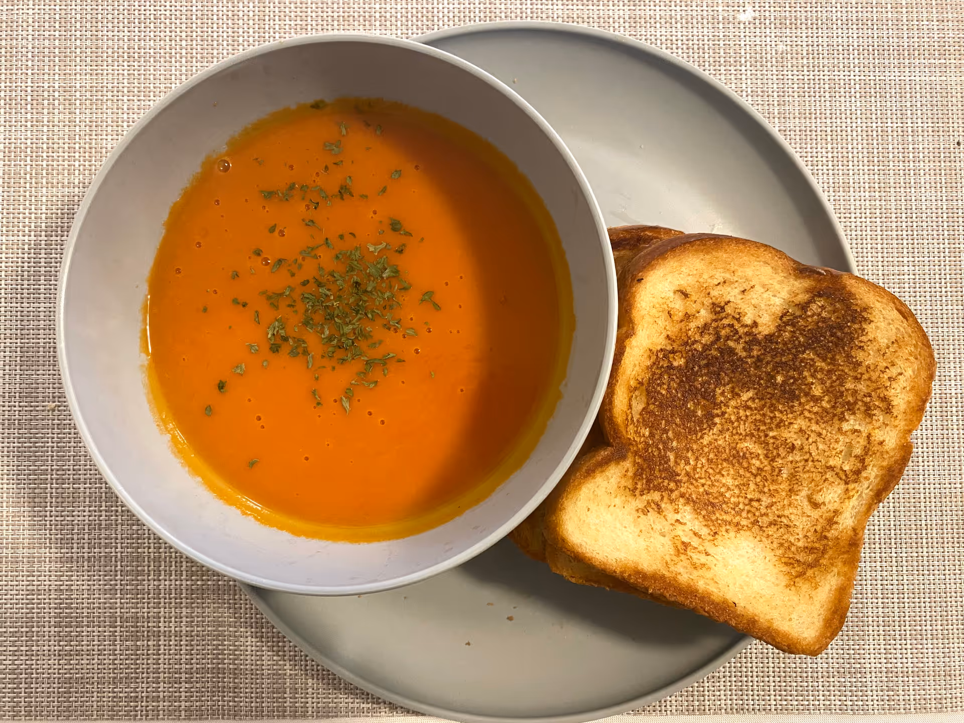 Orange soup garnished with herbs beside toasted bread on a gray plate.