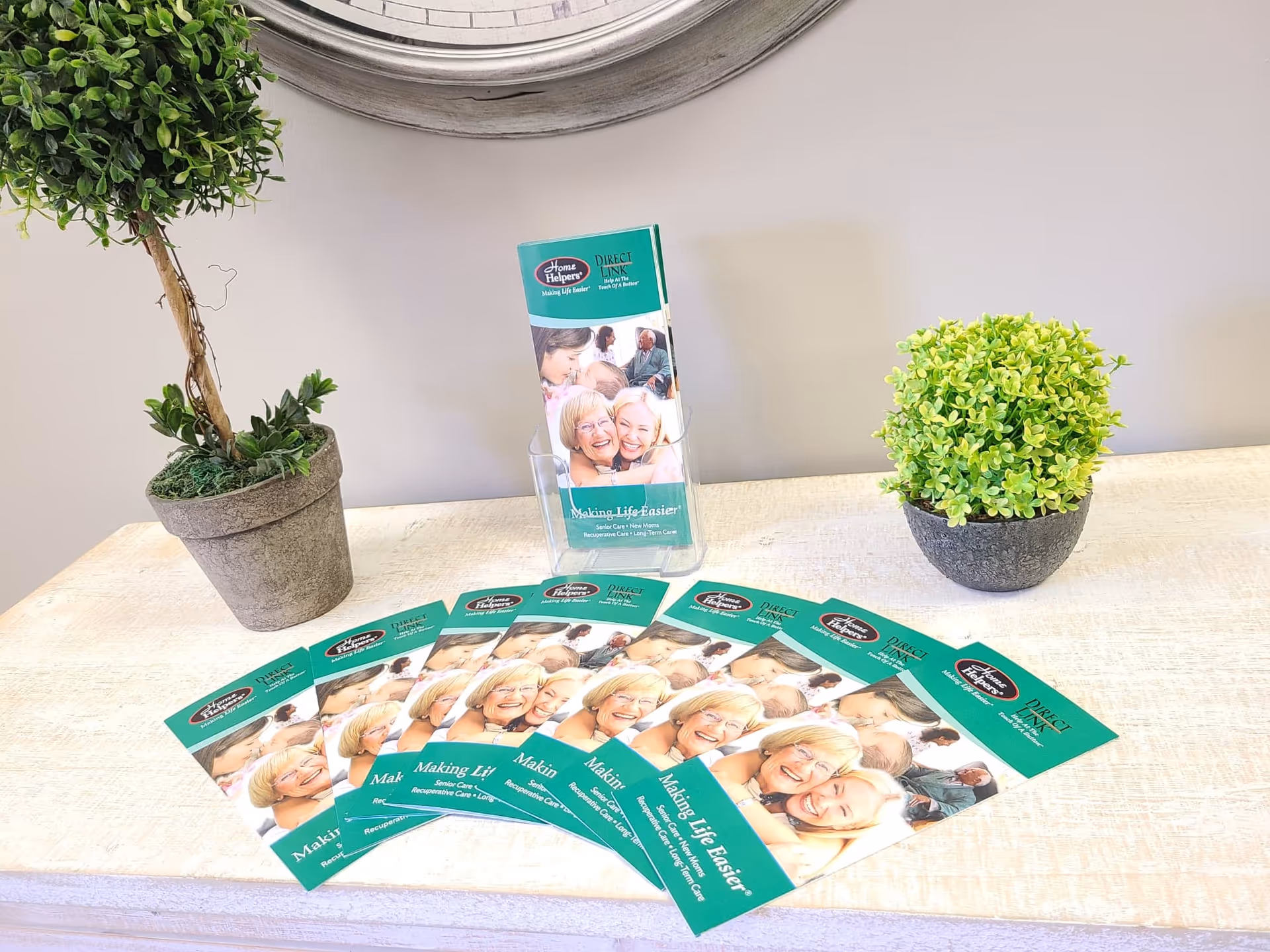 Reception counter with teal Home Helpers brochures and two potted plants.