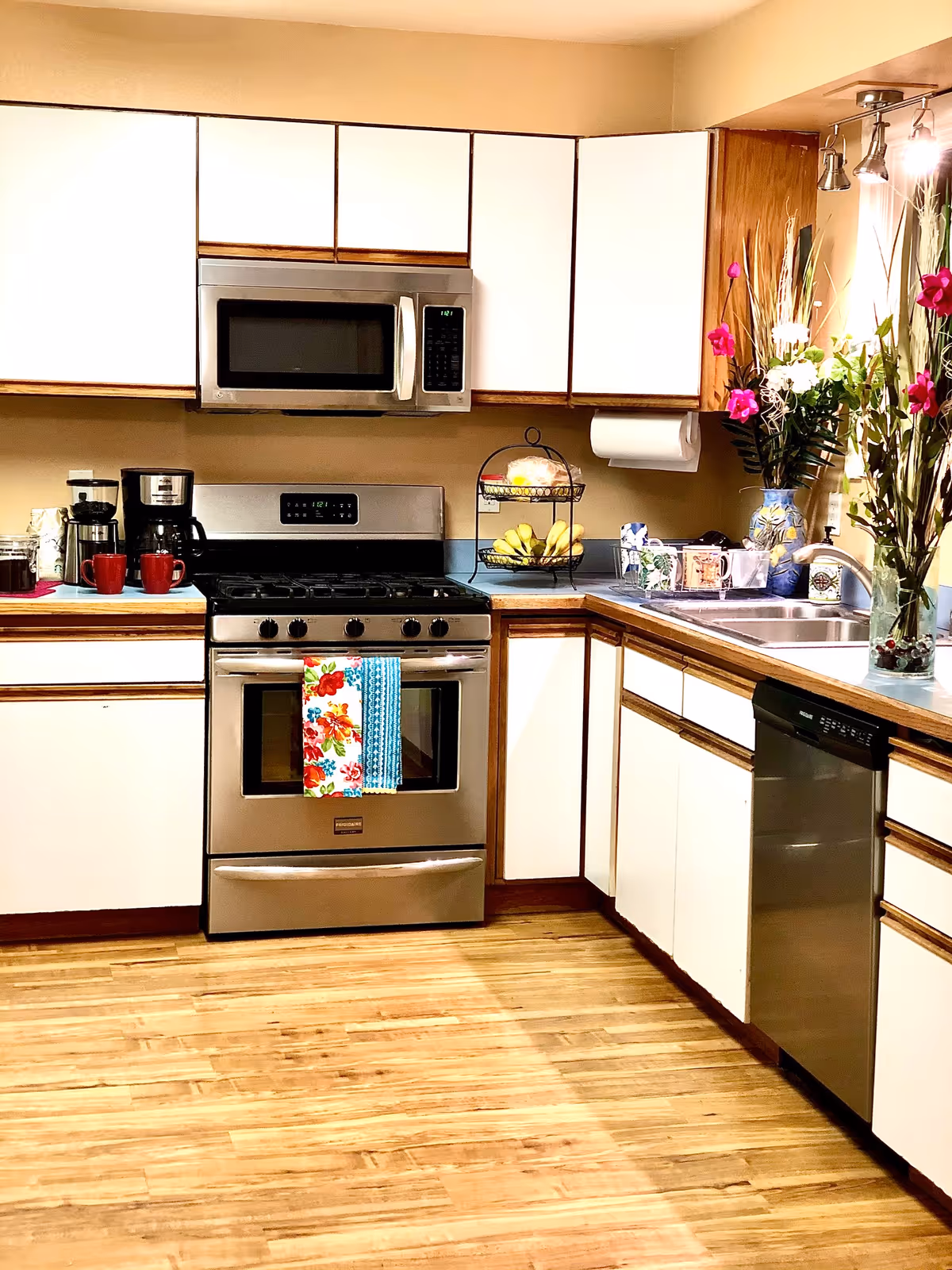 Bright U-shaped kitchen with stainless appliances, white cabinets, and a flower vase.