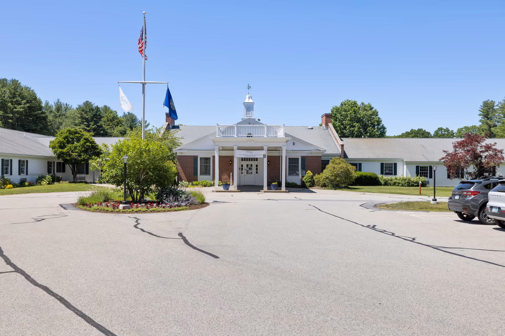 Front view of a single-story senior living facility with parking and flags.