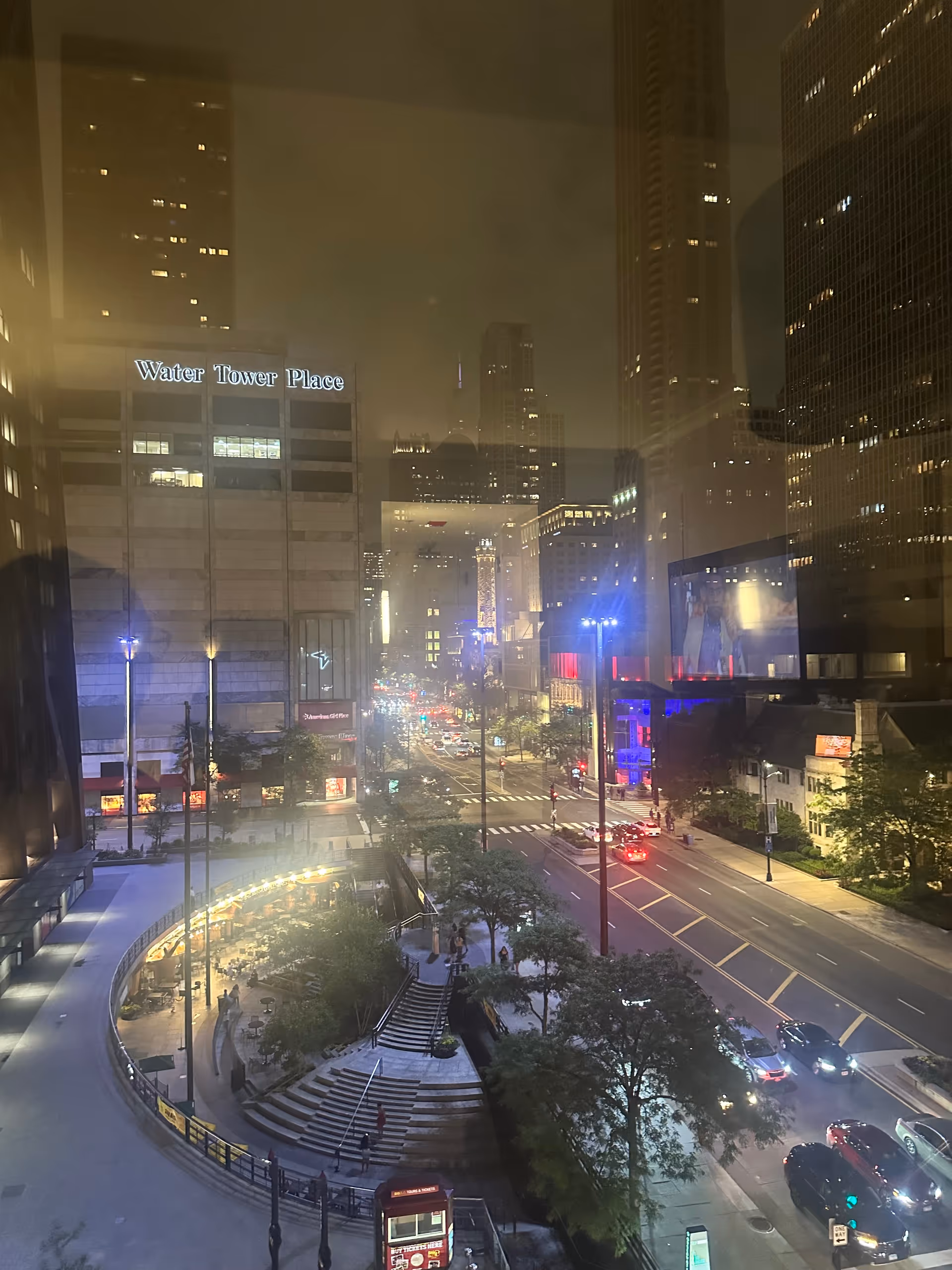 Nighttime cityscape seen through a window, featuring Water Tower Place and a lit downtown street.