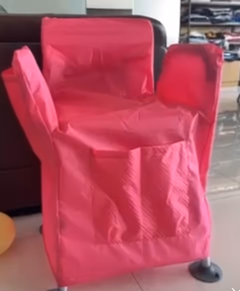 Pink chair with a protective cover on wheels in a bright indoor living area.