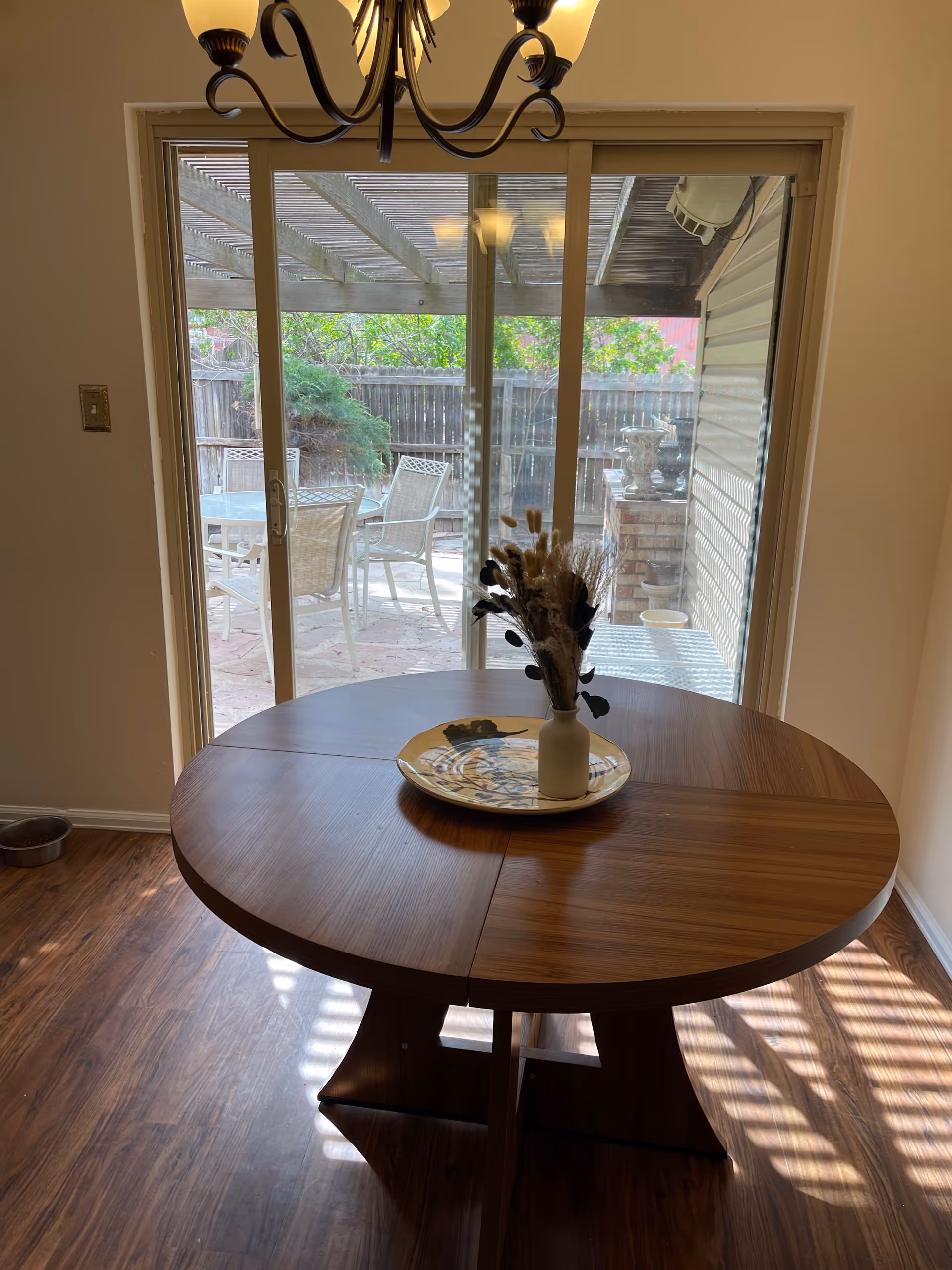 Indoor dining room with a round wooden table, vase centerpiece, and sliding glass doors to patio.