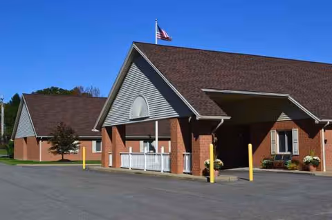 Brick senior care center with a covered entrance and American flag under a blue sky.