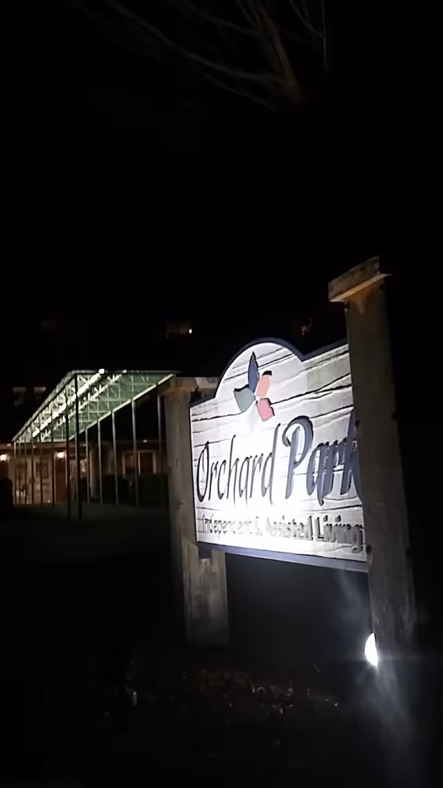 Nighttime exterior of Orchard Park sign at the facility entrance.