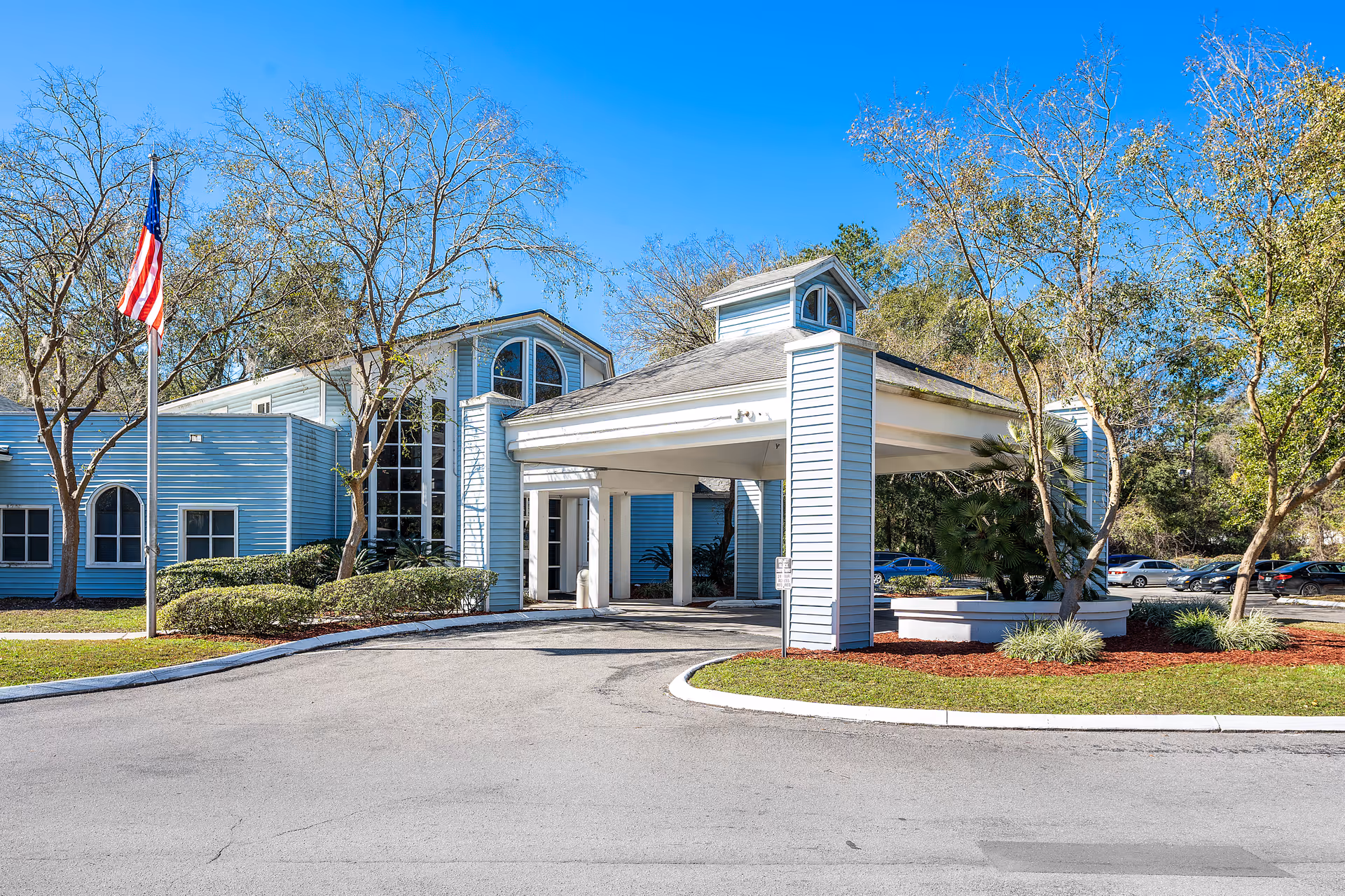 Blue rehab center building with a covered entrance and American flag at a curved driveway.