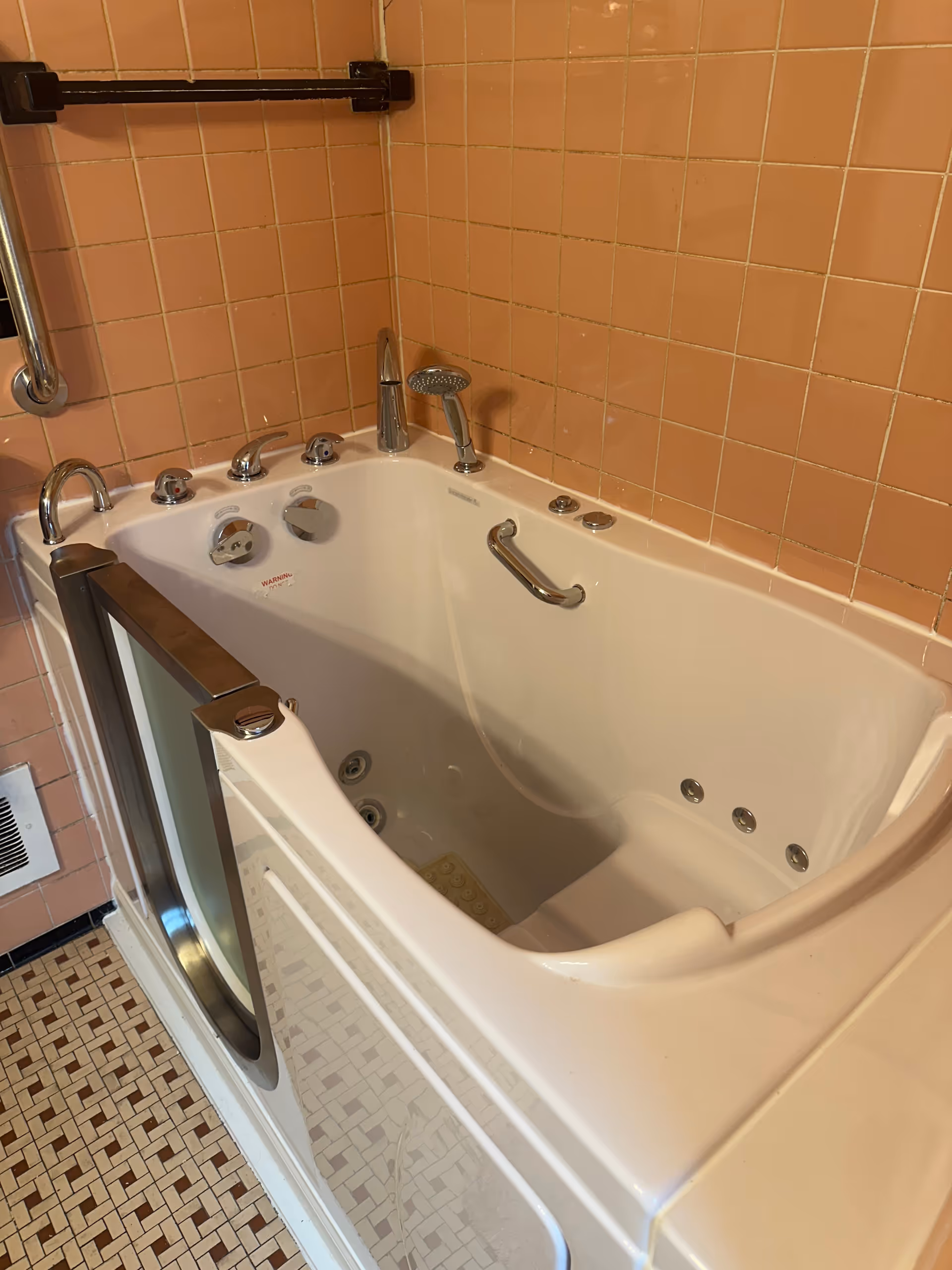 A walk-in jetted bathtub with pink tiled walls and safety rails in a bathroom.